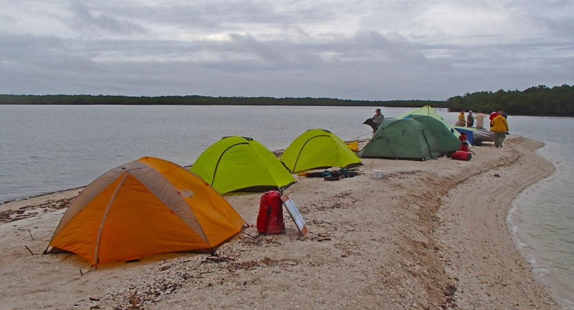 Tents rest on a small sandy peninsula surrounded by water. 